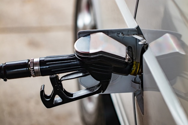 Weißes Auto wird an einer Tankstelle betankt, eine Tankpistole im Einfüllstutzen eines Benzintankwagens.