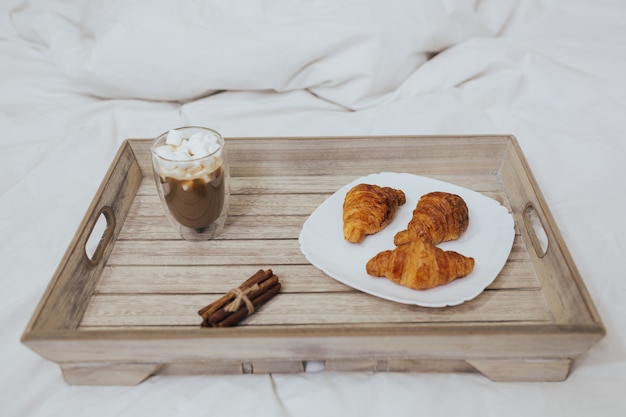 Weißes Bett ein Tablett mit Cappuccino mit Marshmallow und Croissants