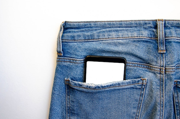 Foto weißes bildschirm-smartphone in der jeanstasche. smartphone platz für text. smartphone in einer tasche auf einem weißen tisch.