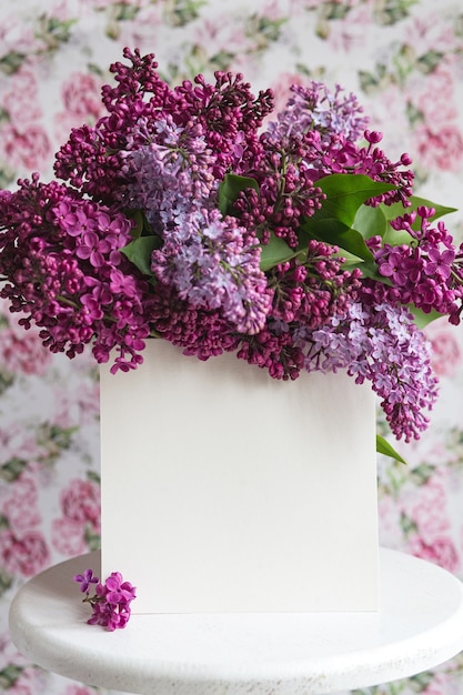 Weißes Blatt in blühenden lila violetten lila Blumen auf einem weißen Ständer auf einem floralen Hintergrund. Grußkarte, Platz für Text, Mock-up