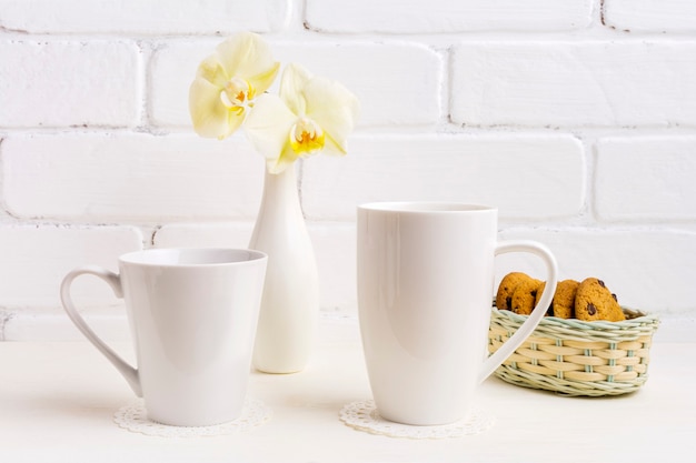 Weißes Cappuccino- und Kaffee-Latte-Becher-Modell mit gelber Orchidee in der Vase und in den Keksen