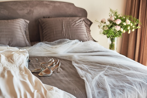 Weißes elegantes Hochzeitskleid, Schleier und Schuhe, die auf dem Bett liegen.