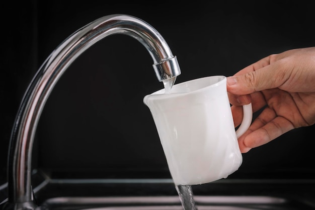 Weißes Glas mit Leitungswasser füllen Moderner Wasserhahn und Waschbecken in der heimischen Küche, die frisches Getränk auf schwarzem Hintergrund gießt Hausarbeit