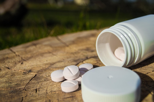 Weißes Glas und weiße Pillen liegen auf einem Stumpf Pillen oder Tabletten in Nahaufnahme mit Bokeh Konzeptfoto zum Thema Coronavirus und Covid19