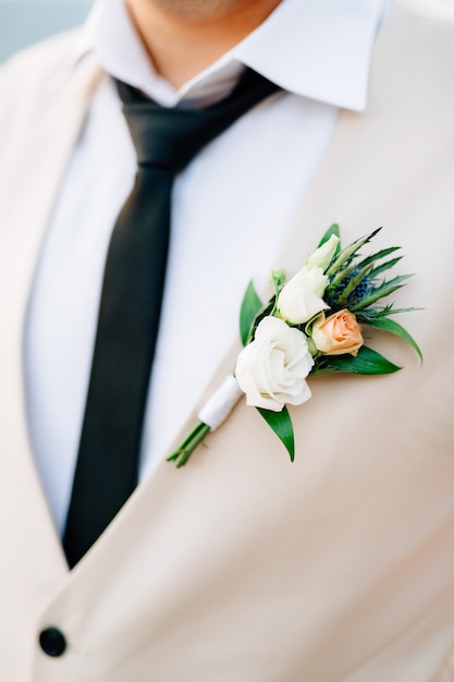 Weißes Hemd, schwarze Krawattenweste und Boutonniere aus Rosen und Eryngium auf der Nahaufnahme des Bräutigams