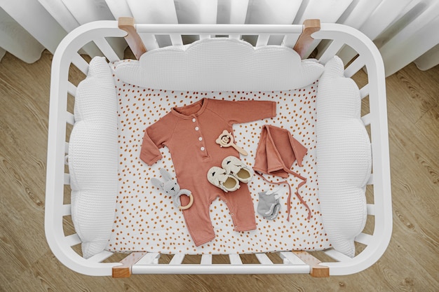 Foto weißes hölzernes babybett mit kissenförmigen wolken im babyzimmer. neugeborene kleidung und accessoires im kinderbett. draufsicht auf das kinderbett