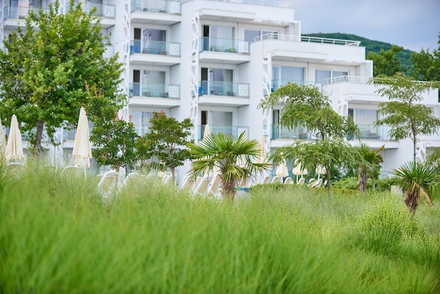 Weißes Hotelgebäude mit vielen Terrassen und grünem Garten im Vordergrund