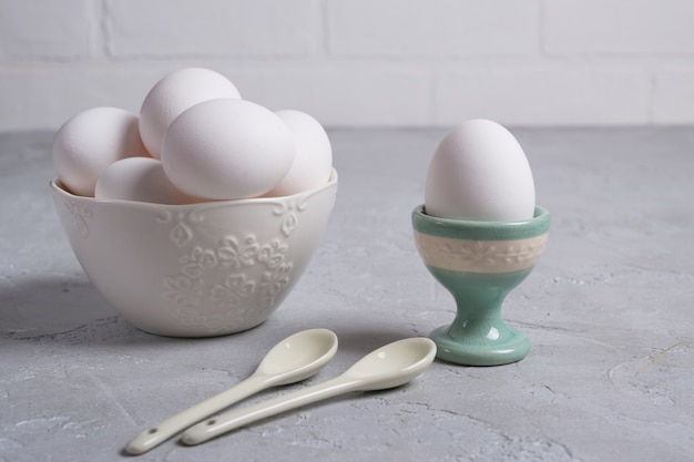 Weißes Hühnerei im Keramikständer und Eier in der weißen Schüssel