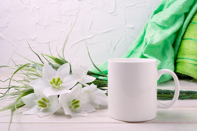 Foto weißes kaffeetassenmodell mit zartem lilienstrauß und grünem schal. leerer becher für designförderung, gestylte vorlage