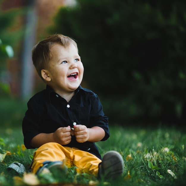Weißes kaukasisches Kind mit einem Lächeln, das im Park auf einem Hintergrund von grünen Bäumen spaziert