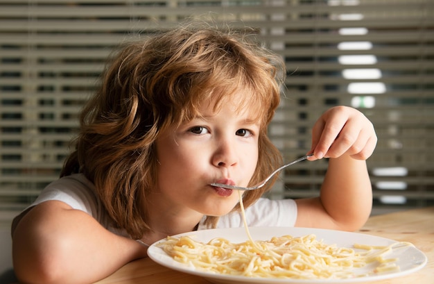 Weißes Kind isst Pasta, Spaghetti, Kinder haben ein lustiges Gesicht.