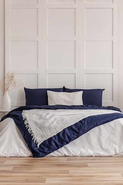 Weißes Kissen in der Mitte eines King-Size-Bettes mit blauer Bettdecke, Kopierplatz an einer leeren Wand