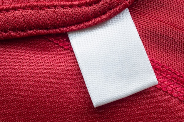 Weißes leeres Wäschepflegekleidungsetikett auf rotem Polyester-Sporthemdhintergrund
