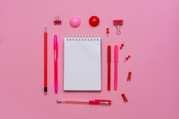 Weißes Notizbuch liegt in Form von leerem auf rosa Hintergrund mit rotem Stift mit Markern Schulbedarf...