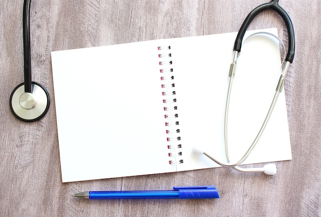 Weißes Notizbuch und ein Stethoskop auf einem grauen Holztisch.