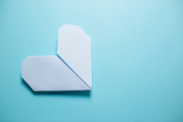 Weißes Origamiherz auf blauem Hintergrund. Valentinstagkarte auf blauem Hintergrund.