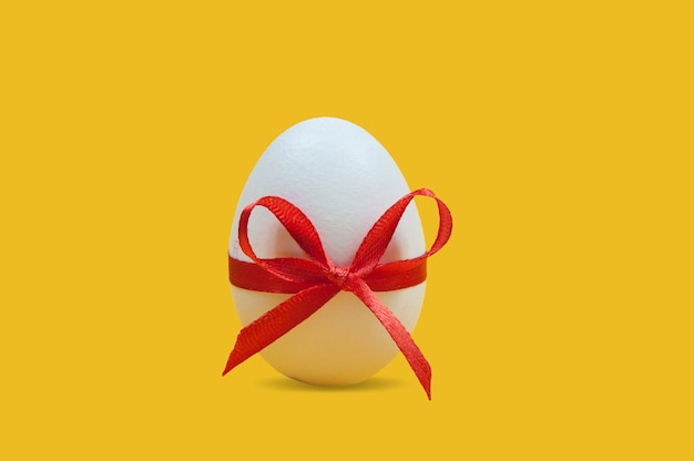 Weißes Osterei gebunden mit einem roten Band mit einer Schleife auf Gelb