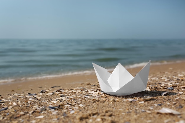 Weißes Papierboot am Sandstrand in der Nähe des Meeres Platz für Text