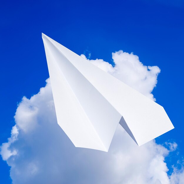 Weißes Papierflugzeug in einem blauen Himmel mit Wolken Das Botschaftssymbol im Boten