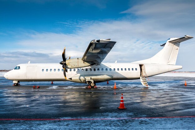 Weißes Passagier-Turboprop-Flugzeug auf dem Vorfeld des Flughafens mit einer offenen Treppenleiter bei kaltem Winterwetter