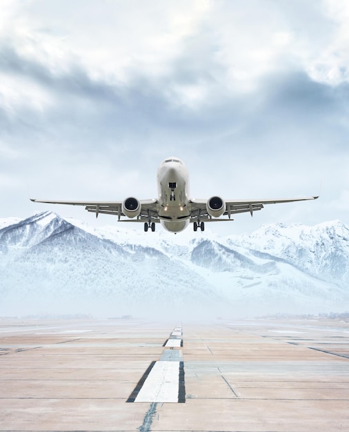 Weißes Passagierflugzeug hebt von der Landebahn vor dem Hintergrund malerischer schneebedeckter Berge ab