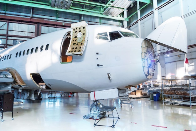 Weißes Passagierflugzeug unter Wartung im Hangar. Überprüfung mechanischer Systeme für den Flugbetrieb. Das Flugzeug hat Wetterradar geöffnet