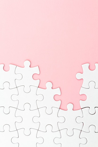 Weißes Puzzlespiel über rosa Hintergrund mit fehlenden Stücken. Unvollständige Elemente, Lösungssuchkonzept