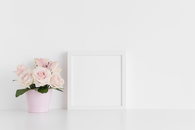 Weißes quadratisches Rahmenmodell mit rosa Rosen in einem Topf auf einem weißen Tisch