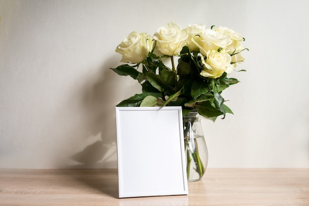 Weißes Rahmenmodell des Porträts auf Holztisch. Moderne Vase mit Rosen. Skandinavisches Interieur. Foto in hoher Qualität