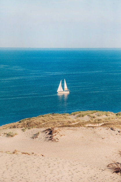 Weißes Segelboot Auf dem Hintergrund der Dünen und des blauen Himmels im Meer. Weißes Segelboot in der Ostsee. Lithuania.Nida.