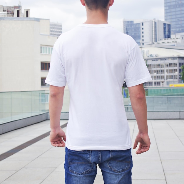 Weißes T-Shirt Mockup Rückansicht junger Mann, der ein weißes T-Shirt auf einem verschwommenen Stadthintergrund trägt