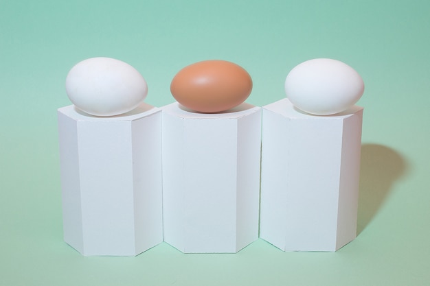 Weißes und braunes Ei auf grünem Hintergrund. Weiße geometrische Formen und Eier. Osterferien. Isoliert