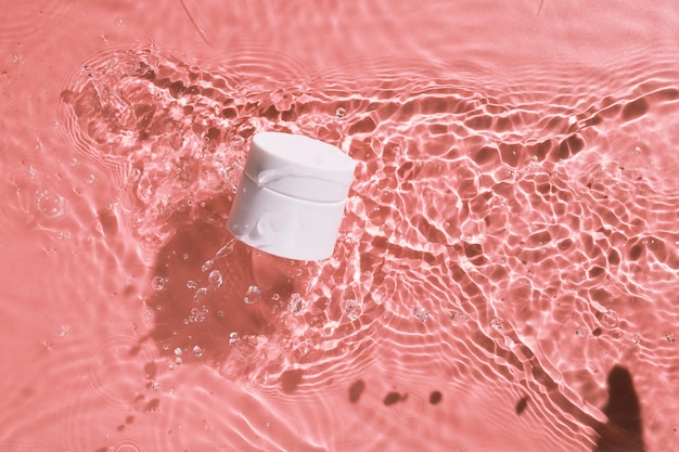 Weißes und leeres Kosmetikcremeglas ohne Markenzeichen auf der rosafarbenen Wasseroberfläche. Branding-Mockup für leere Etiketten