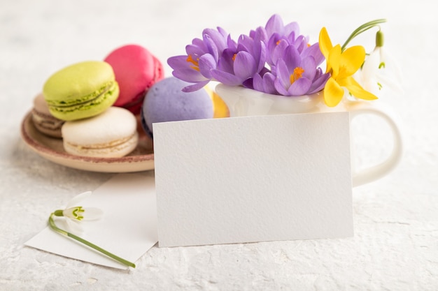 weißes Visitenkartenmodell mit Frühlingskrokusblüten und Makronen auf grauem Betonhintergrund.