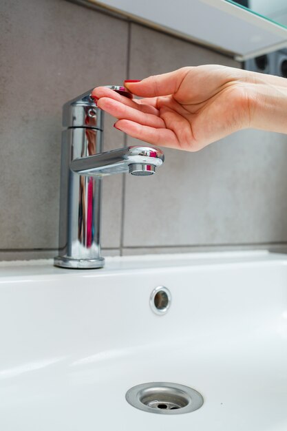 Weißes Waschbecken mit silbernem Wasserhahn im Badezimmer. Graue Dose mit Flüssigseife für die Hände. Leitungswasser aufdrehen, persönliche Händehygiene