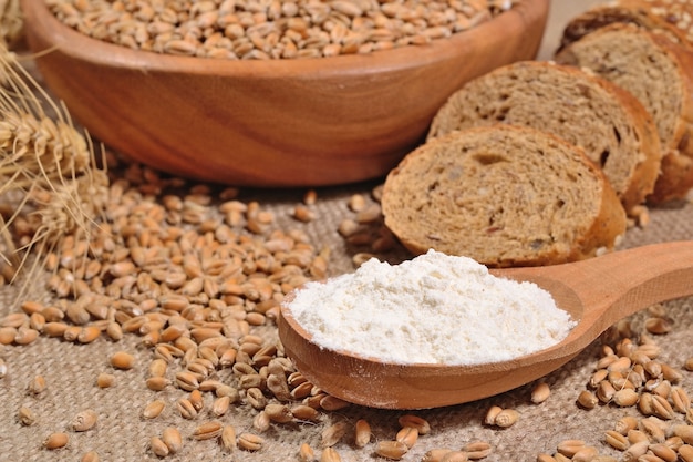 Weißmehl in einem Holzlöffel, Weizen und Brot auf einem Sack Hintergrund