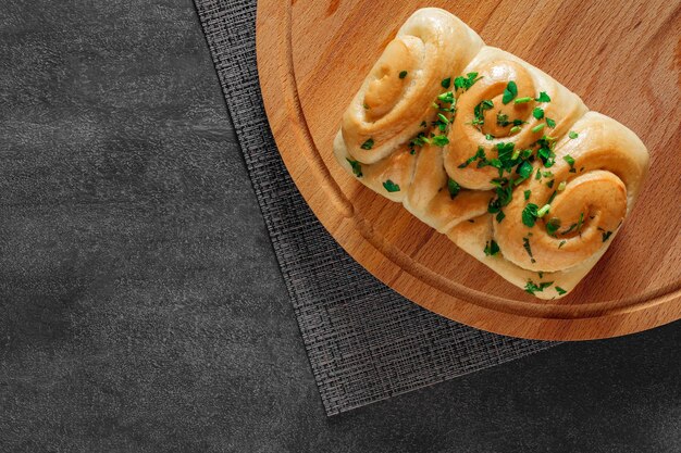 Weißteigbrot mit Knoblauch und Kräutern auf einem runden Holzbrett mit dunklem Hintergrund, Draufsicht