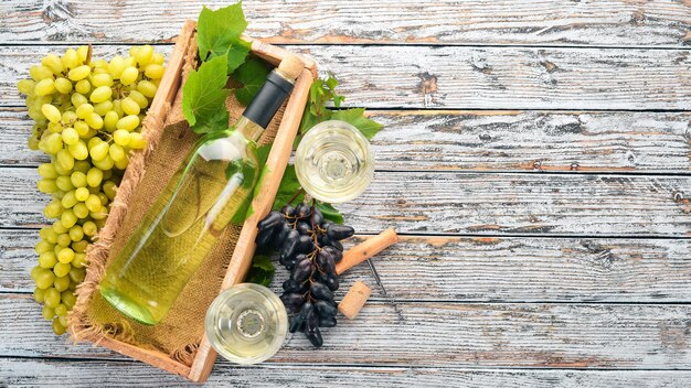 Weißwein in einer Flasche mit Glas und Trauben auf weißem Holzhintergrund Freier Platz für Text Ansicht von oben