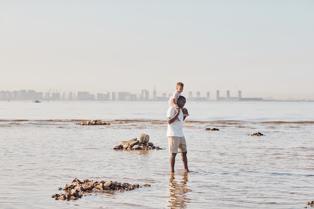 Weitwinkel-Minimalporträt eines glücklichen jungen Vaters und seines Sohnes, die gemeinsam am Strand spazieren gehen und ...