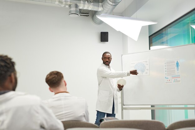 Weitwinkelansicht des afroamerikanischen Mannes, der am Whiteboard steht, während er ein Seminar über Medizin im College hält, Kopierraum