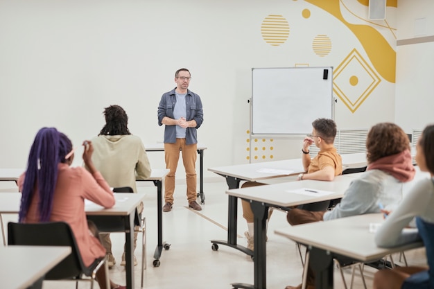 Weitwinkelansicht eines reifen männlichen Lehrers, der der Klasse junger Schüler in der modernen Schule einen Vortrag hält, Kopierraum