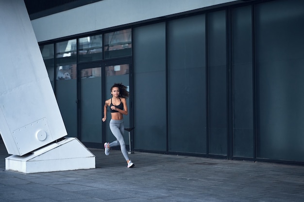 Weitwinkelaufnahme einer jungen athletischen Dame, die im Stadtstadion mit städtischer Glaslage läuft