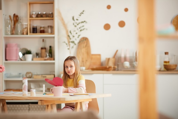 Weitwinkelporträt des niedlichen Mädchens, das Herzformkarte hält, während am Tisch im gemütlichen Innenraum sitzen, Raum kopieren