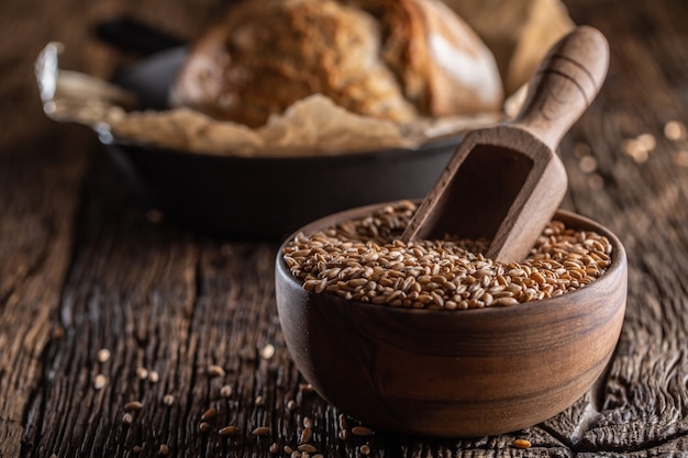 Weizenkörner - die hauptzutat des brotes, das in eine holzschale gefüllt und eine rustikale holzschaufel tief eingenäht ist. im hintergrund knuspriges brot backen.