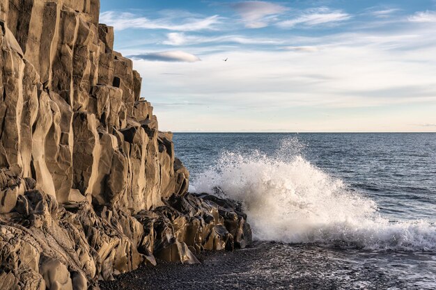 Foto welle, die auf die halsanefhellir-höhle mit basaltgesteinbildung am schwarzen sandstrand am strand von reynisfjara trifft