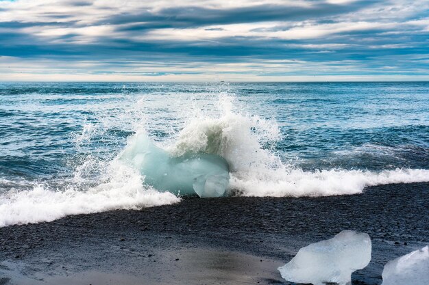 Welle stürzt mit Eisberg auf schwarzem Sandstrand in Diamond Beach während des Sommers im Süden Islands