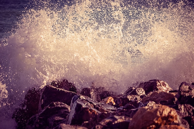 Welle traf den Felsen am Strand, Meerwasserspritzer sprühen bei Sonnenuntergang.