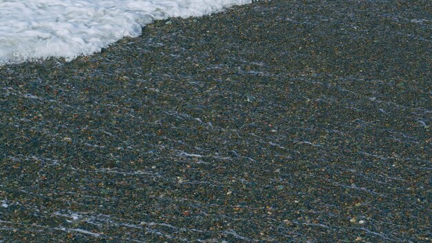 Wellen brechen auf dem Kiesstrand, Wellen surfen auf dem Strand, Wellen waschen den Kiesstrand in langsamer Bewegung.
