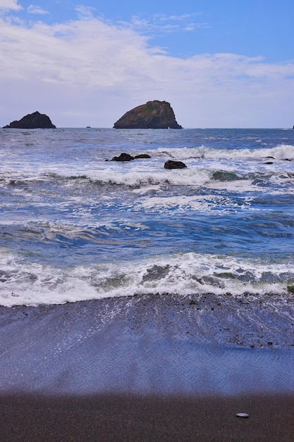 Wellen, die den schwarzen Sandstrand an der Westküste treffen