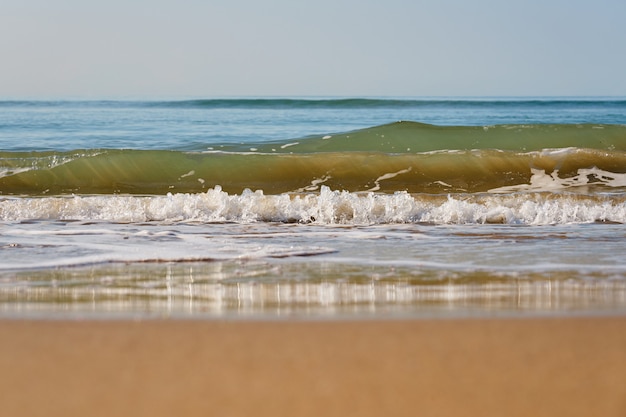 Wellen mit Schaum an einem Sandstrand.